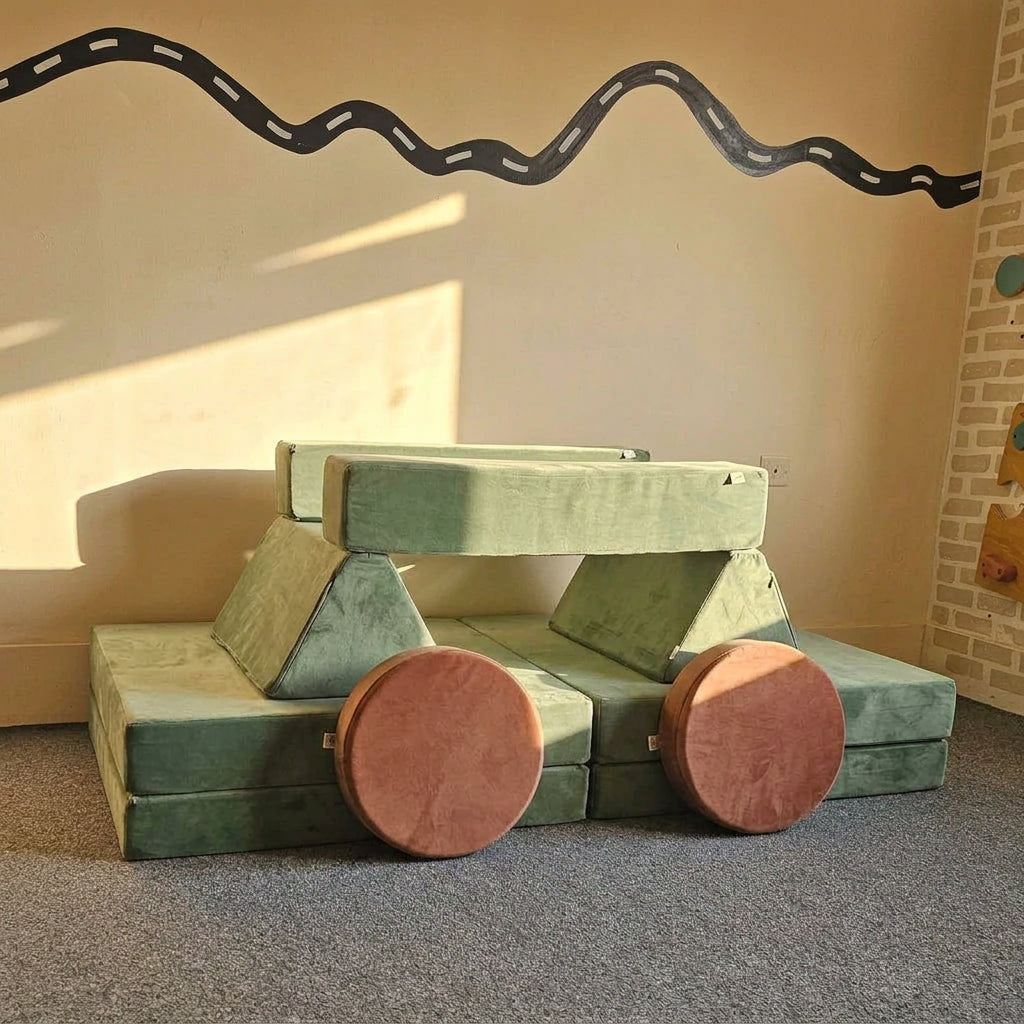 A blue modular play couch with two round yellow cushions, photographed in an indoor room with a beige wall, gray carpet, and a black wavy line decoration on the floor.